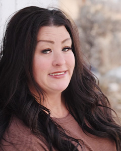 Woman with long dark hair, wearing a brown top, poses for portrait with slight smile.