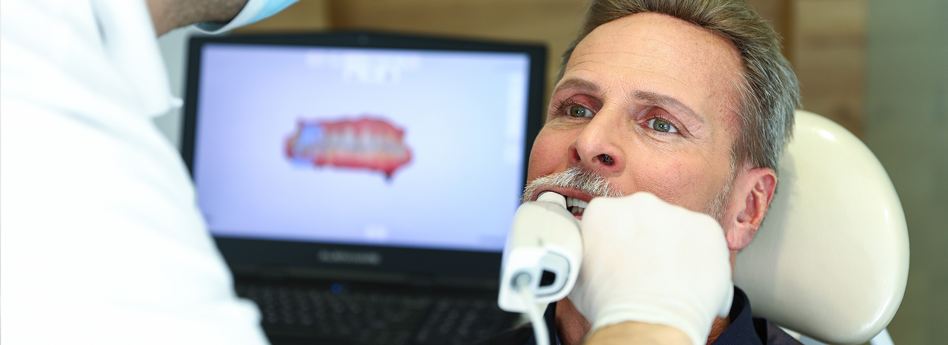 An elderly man receiving dental care with a medical professional using a computer screen.