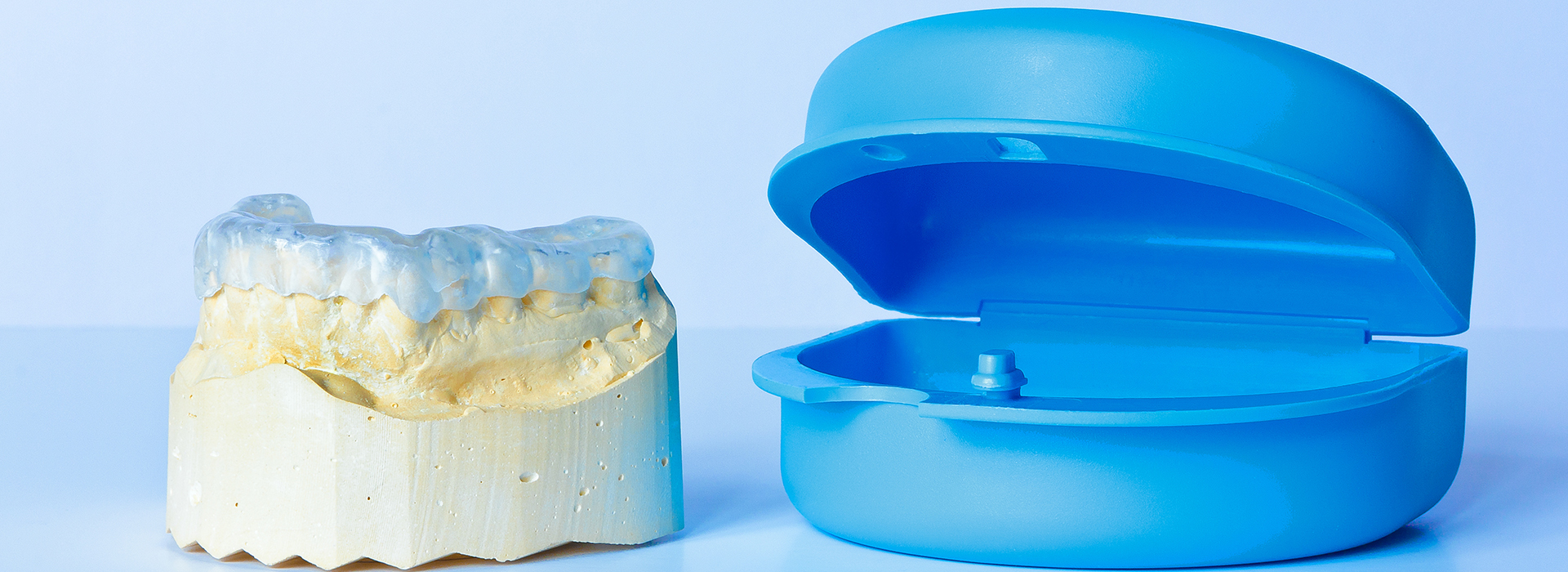 An image showing two dental implants one blue and one yellow, alongside a transparent plastic ring on a white surface.